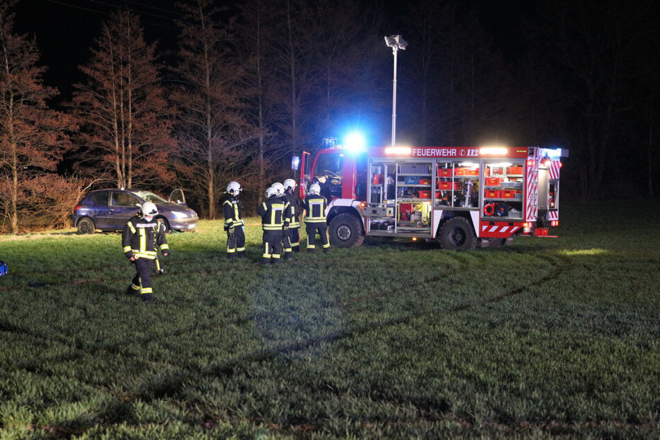 Kameraden der Feuerwehr stehen auf einem Feld in Reichweite des verunfallten Peugeots.