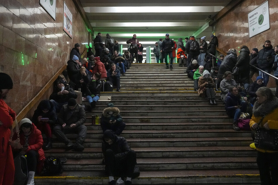 Menschen sitzen auf Treppen in einer U-Bahn-Station in Kiew, die während eines Raketenangriffs als Luftschutzbunker genutzt wird.