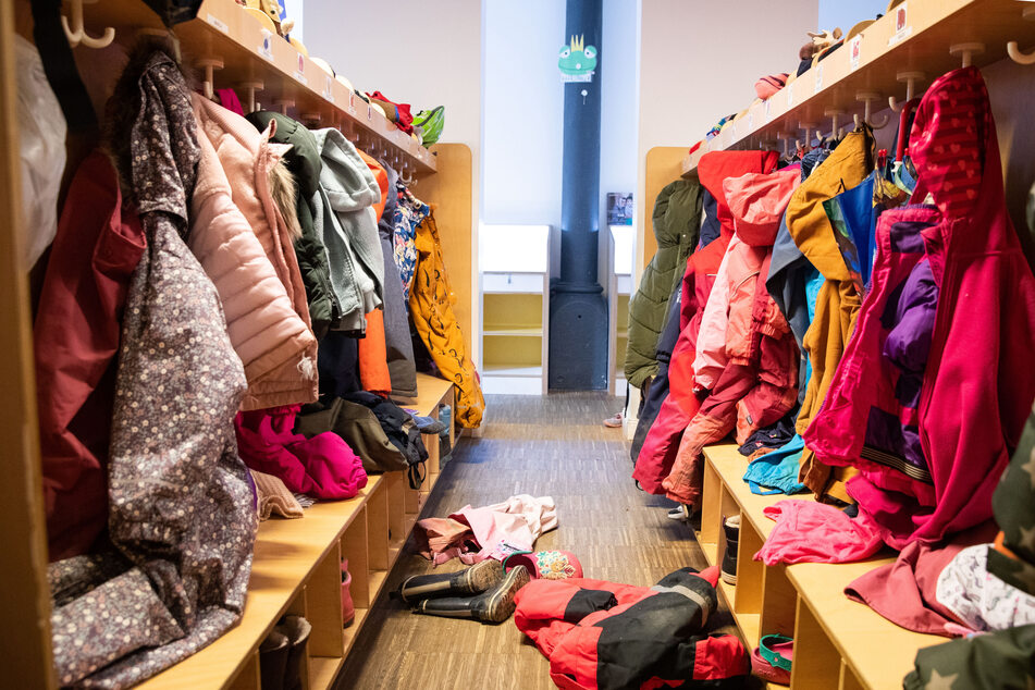 Blick über die Garderobe mit Jacken, Mützen und anderen Kleidungsstücken in einem Kindergarten.
