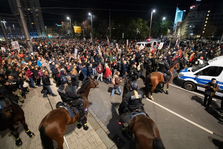 07.11.2020, Sachsen, Leipzig: Teilnehmer stehen nach dem Ende einer Demonstration der Stuttgarter Initiative "Querdenken" am Hauptbahnhof hinter der Reiterstaffel der Polizei.