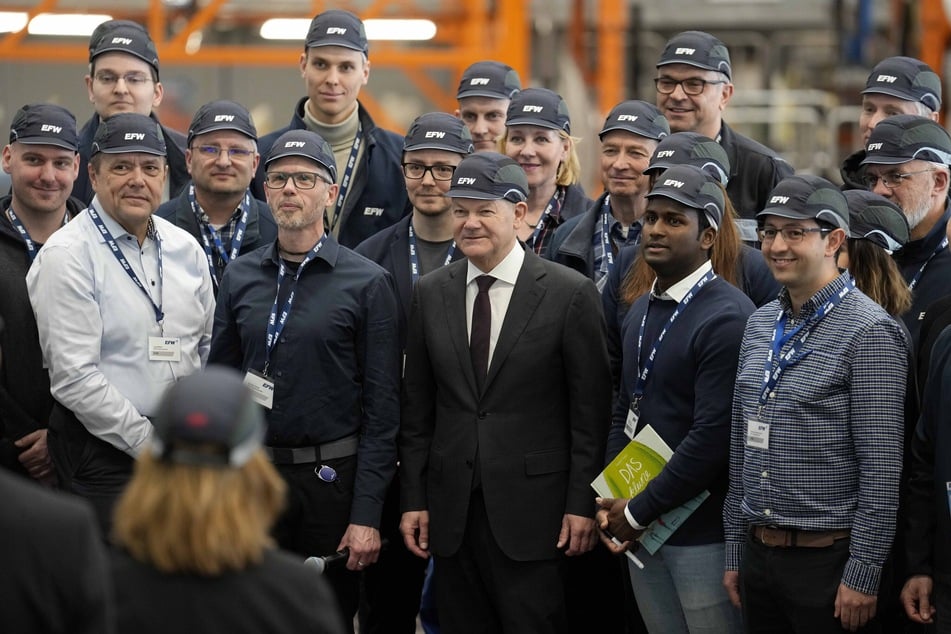Bundeskanzler Olaf Scholz (65, SPD, M.) steht bei seinem Besuch der Elbe Flugzeugwerke in einem Hangar mit Mitarbeitern der Flugzeugwerke zusammen.
