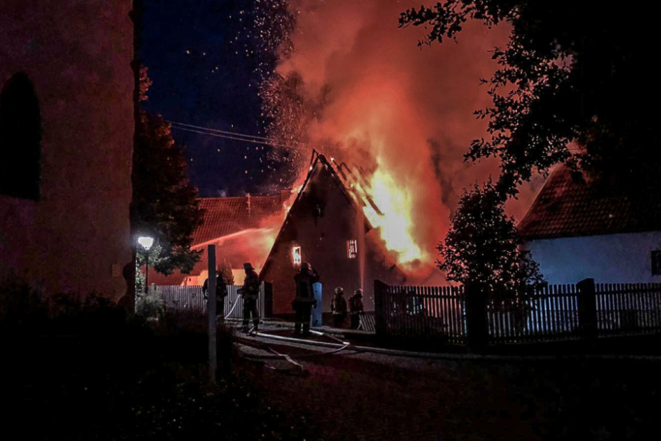 Meterhohe Flammen schlagen aus dem Haus. Feuerwehrleute kämpfen gegen die Flammen an.