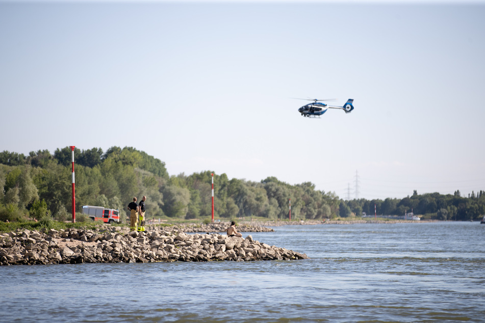 Aus einem Hubschrauber und vom Ufer aus suchen Einsatzkräfte nach einem verschollenen Schwimmer im Rhein.
