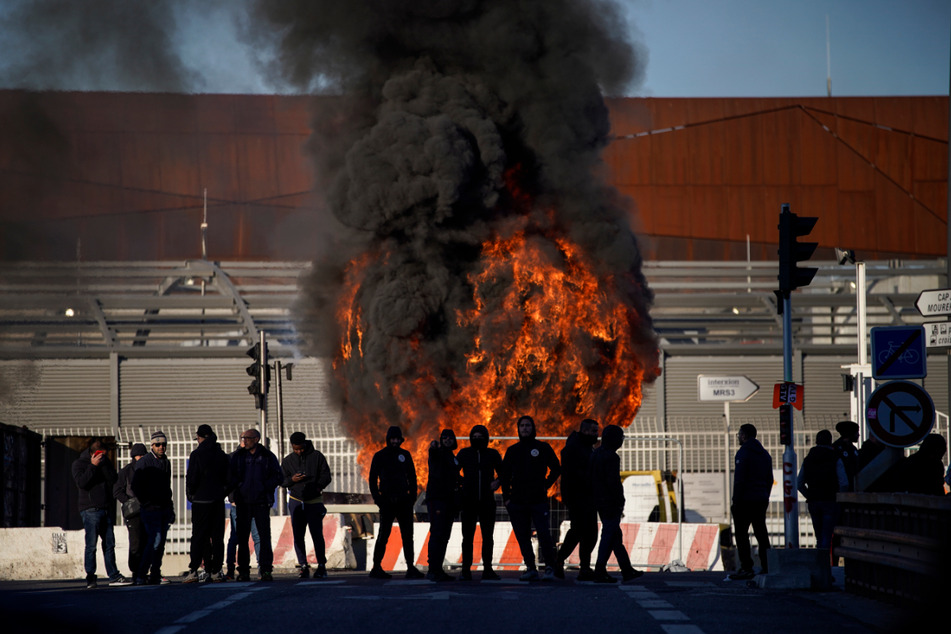 Hafenarbeiter stehen vor einer brennenden Barrikade im Hafen von Marseille.