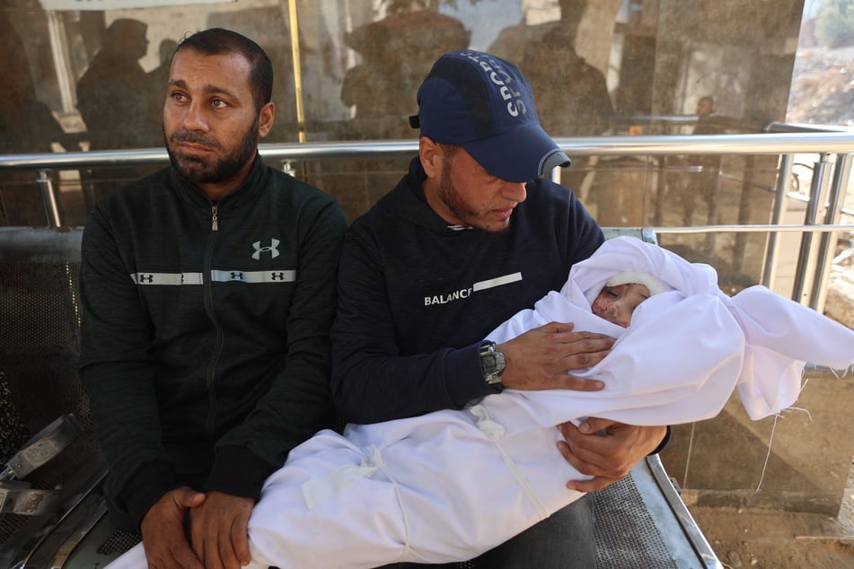 A displaced Palestinian man holds the body of his child, killed in Israeli strikes, at Al-Shifa Hospital in Gaza City on November 20, 2025.