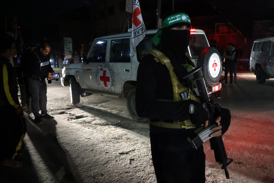 Ein Hamas-Kämpfer steht Wache, während eine Fahrzeug des Roten Kreuzes freigelassene Geiseln nach Israel bringt.