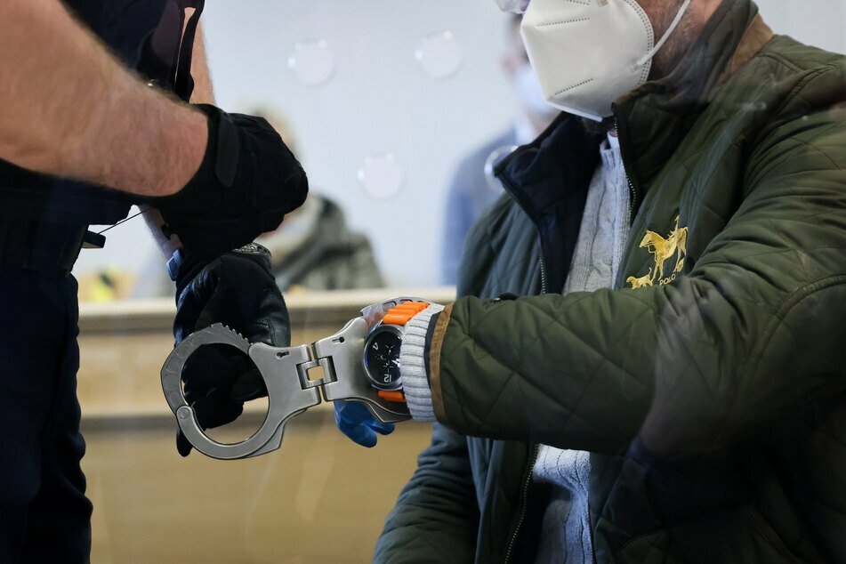 Ein Justizbeamter nimmt dem Angeklagten die Handschellen ab.