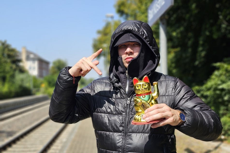 Rapper und TikToker Fydoz steht mit einer Winkekatze auf dem Bahnhof in Bad Köstritz. Sein Ziel: Mit kurzen Clips den Osten von Deutschland pushen.