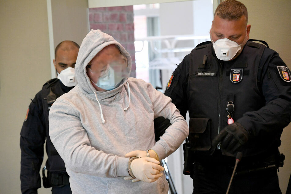 Der Angeklagte (47) wird mit Maske und Handschuhen in den Gerichtssaal geführt.