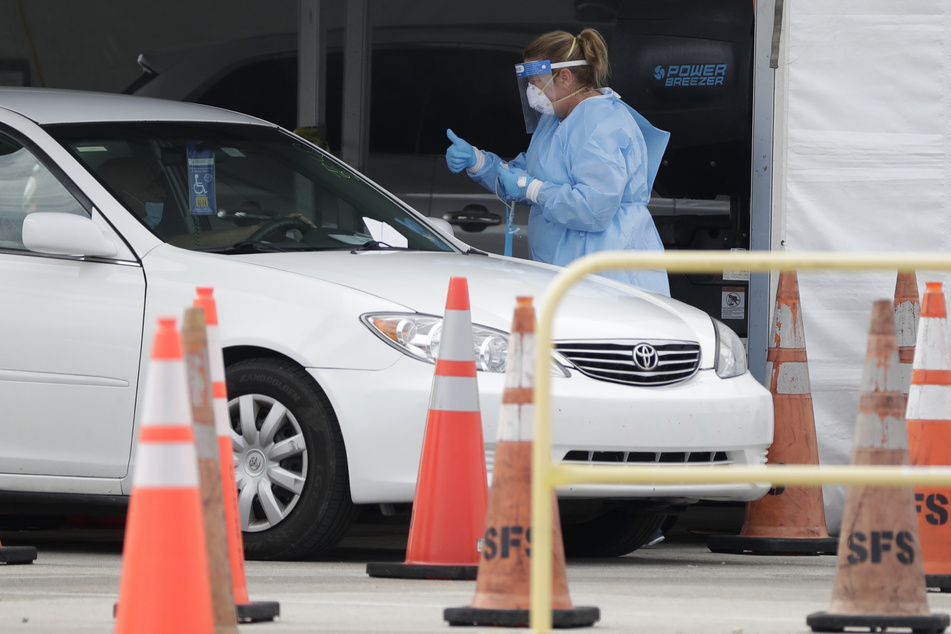 Eine medizinische Mitarbeiterin in Schutzkleidung zeigt einem Autofahrer in einer provisorischen Teststation einen Daumen nach oben.