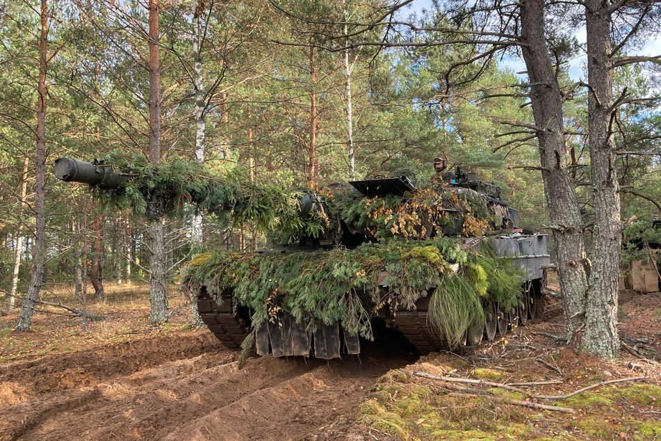 Ein Leopard-Panzer steht bei der Militärübung "Iron Wolf ll" in Litauen getarnt im Wald. Zum besseren Schutz des Baltikums und zur Stärkung der Nato-Ostflanke führt die Bundeswehr seit fünf Jahren einen Nato-Gefechtsverband in Litauen.