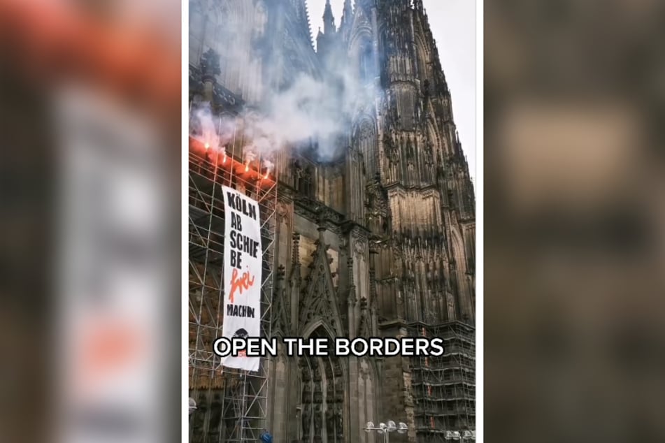 Mit einem Plakat und vier "Bengalischen Feuern" protestieren am Samstag Aktivisten auf einem Gerüst am Kölner Dom.