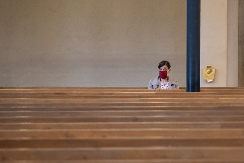 Eine Frau mit Mundschutz verfolgt einen Gottesdienst in der ansonsten fast menschenleeren St. Matthäuskirche.
