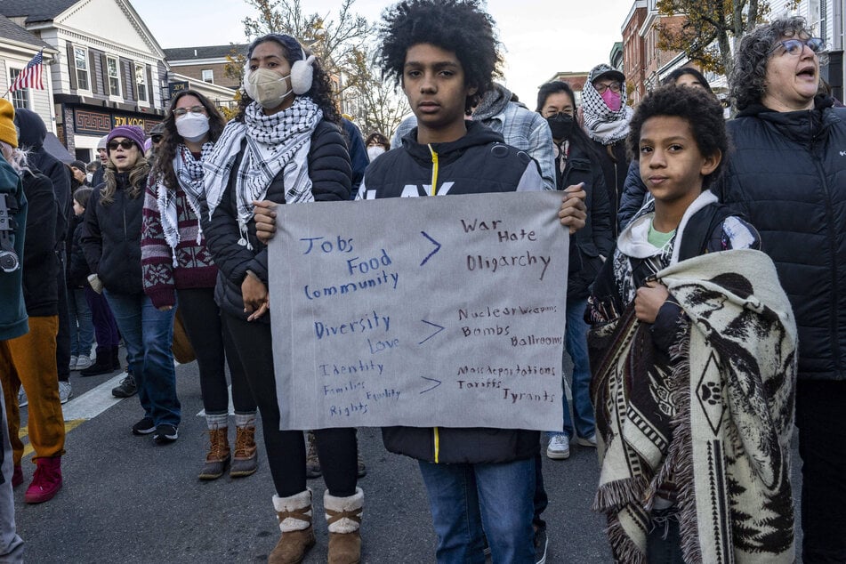 Youth hold a sign opposing "war," "hate," and "oligarchy" while other participants wear keffiyehs during the 2025 National Day of Mourning.