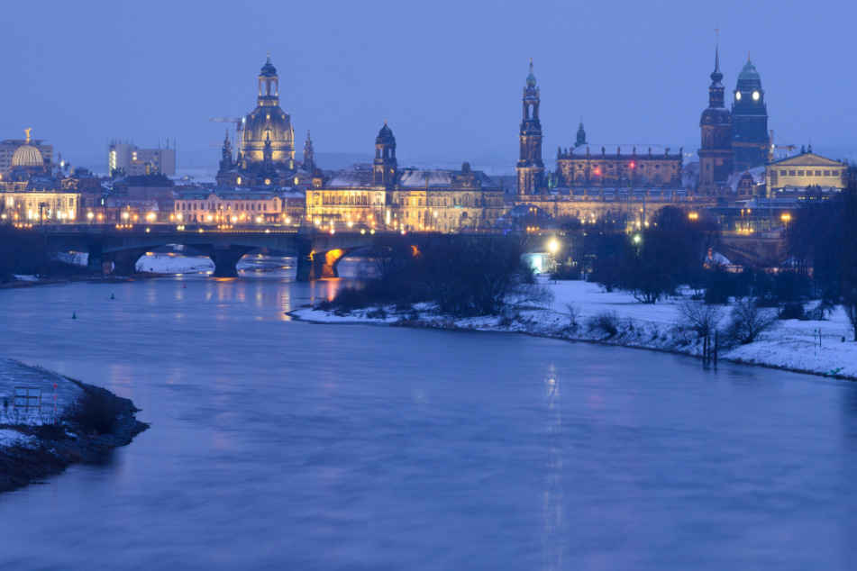 Die Ufer der Elbe sind vor der Dresdner Altstadt mit der Kuppel der Kunstakademie, der Frauenkirche, dem Ständehaus, der Katholischen Hofkirche, dem Hausmannsturm, dem Rathausturm und der Semperoper mit Schnee bedeckt.