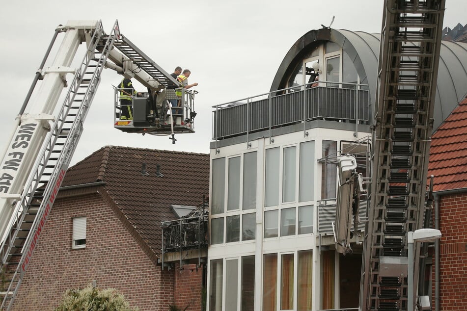 Feuerwehrleute stehen an einem beschädigten Wohnhaus auf einer Drehleiter.