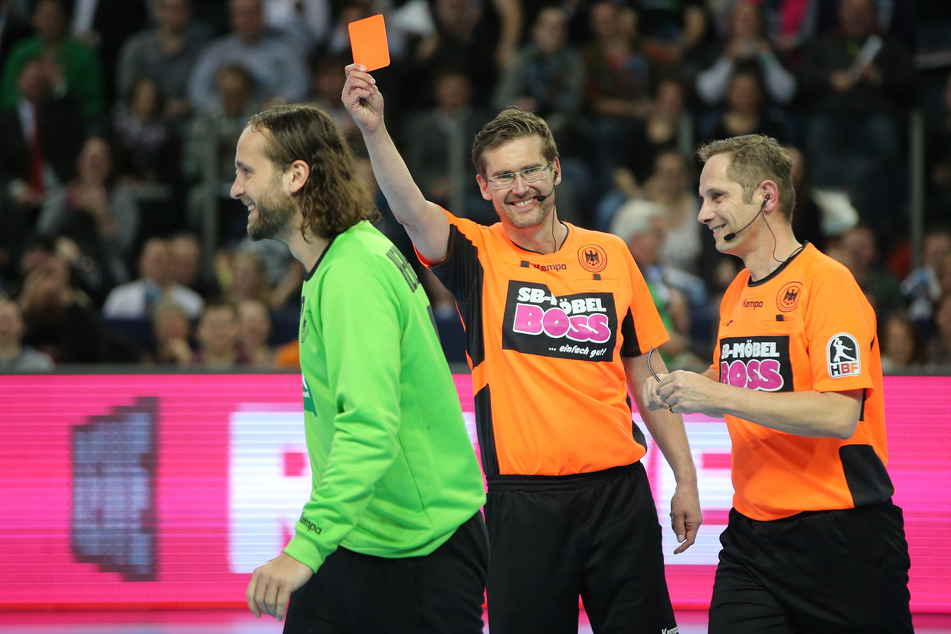 Der Schiedsrichter Lars Geipel (M) zeigt dem Nationaltorwart Silvio Heinevetter (l.) bei einem Handball Allstar Game aus Spaß die rote Karte. Rechts ist der Schiedsrichter Marcus Helbig zu erkennen.