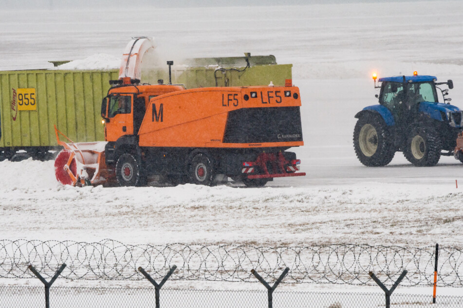 Eine Schneefräse, ein Containerfahrzeug und ein Traktor mit Schneepflug befreien eine Startbahn auf dem Flughafen München am Sonntag vom Schnee.