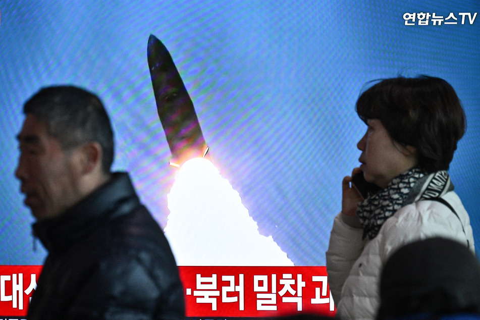 People walk past a television showing a news broadcast with file footage of a North Korean missile test, at a train station in Seoul on March 18, 2024.