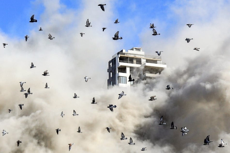 A flock of pigeons flies away as a smoke cloud erupts after a rocket fired by an Israeli war plane hit a building in Beirut's southern suburb of Shayah on October 22, 2024.