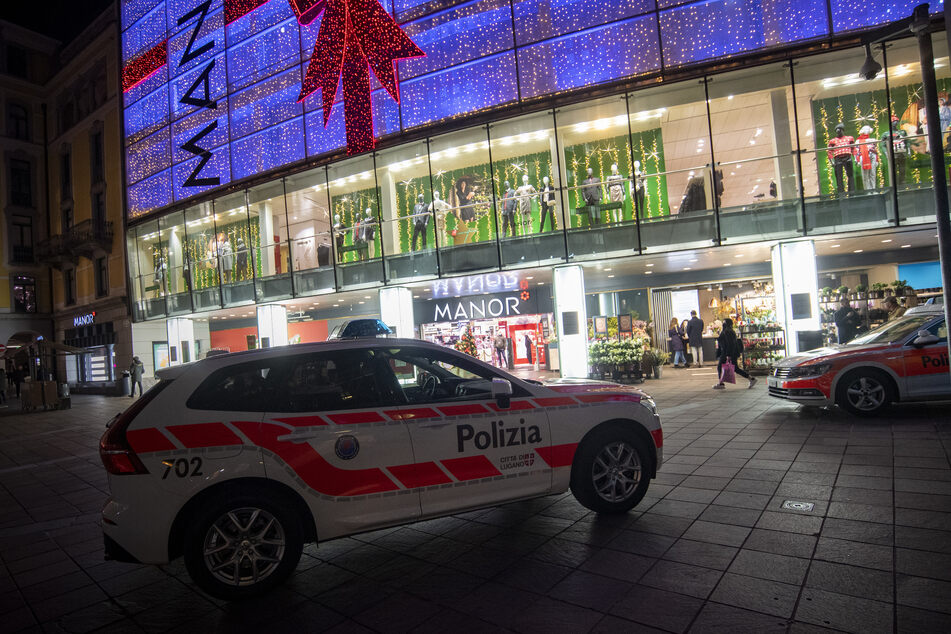 Polizeifahrzeuge stehen vor dem Kaufhaus Manor an der Piazza Dante im schweizerischen Kanton Tessin. Eine Frau dort zwei Passantinnen mit einem Messer angegriffen.