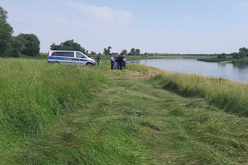 Polizisten stehen am Ufer rund 500 Meter flussabwärts vom Fähranleger entfernt und blicken auf den Fluss - bis hierhin trieb der untergegangene Wagen.