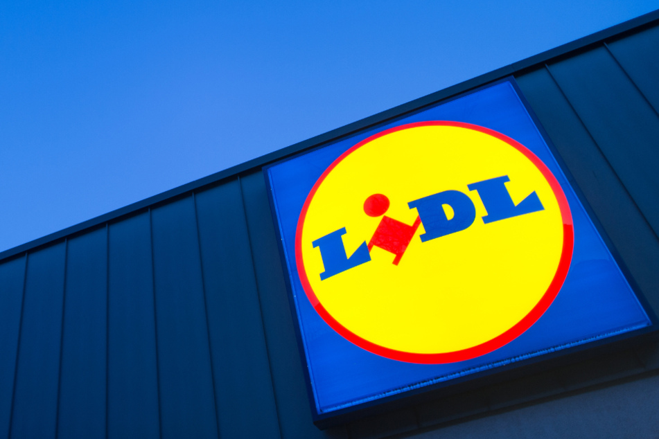 Das Logo eines Lidl-Supermarktes in Berlin-Reinickendorf leuchtet vor dem Abendhimmel.