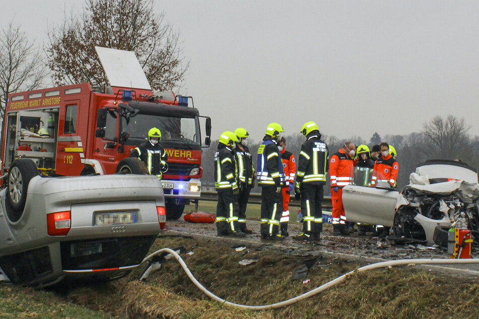 Rettungskräfte stehen am Unfallort an den Wracks der zwei Autos.