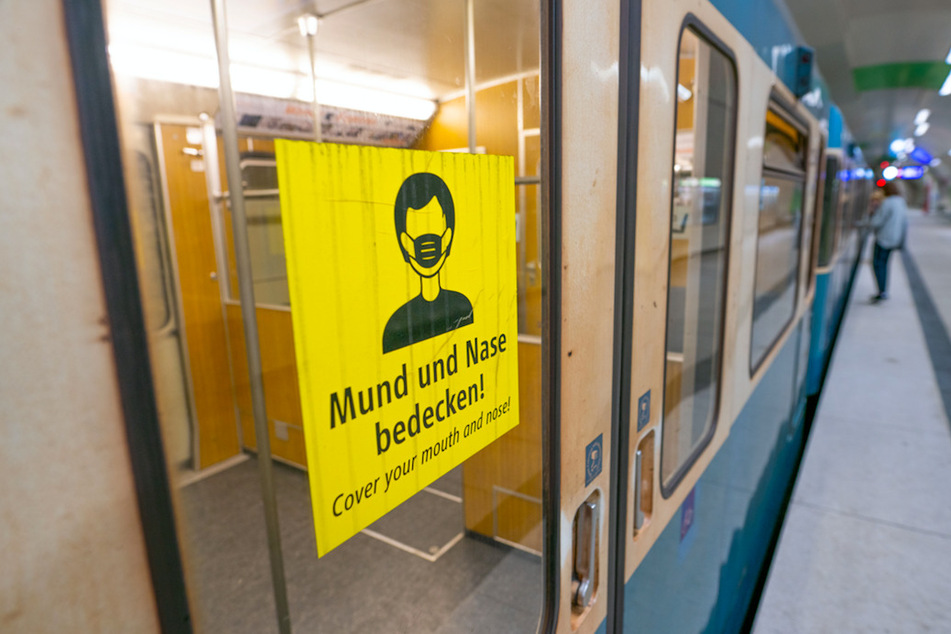"Mund und Nase bedecken!" steht in Deutsch und Englisch auf einem Schild an einem Waggon der Münchner U-Bahn.