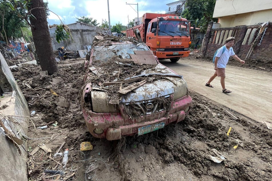 Un hombre pasa junto a un coche cubierto de escombros en Filipinas.
