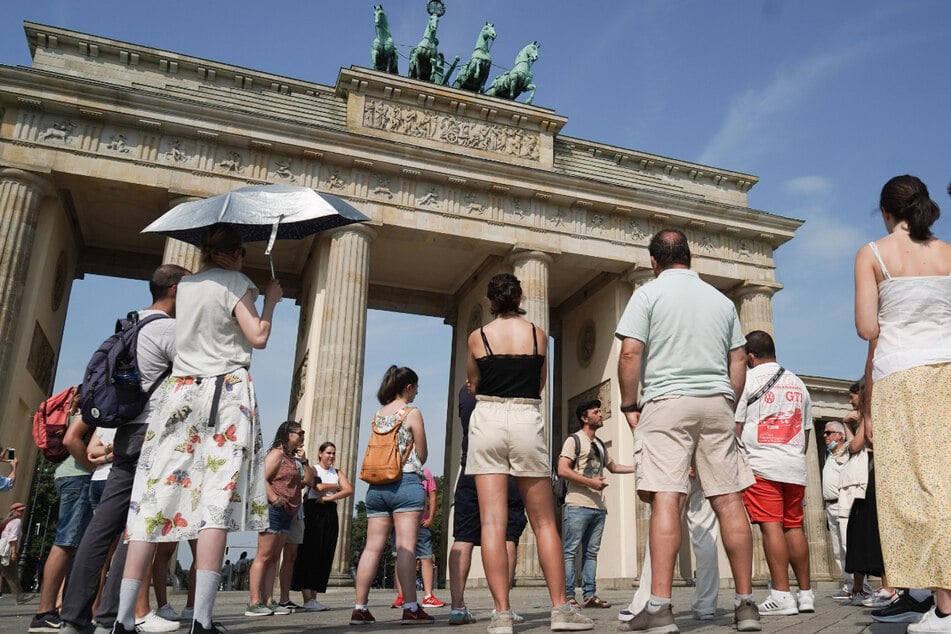 Mit einem silbernen Regenschirm schützt sich die Teilnehmerin einer Stadtführung vor dem Brandenburger Tor vor den Strahlen der Sonne.