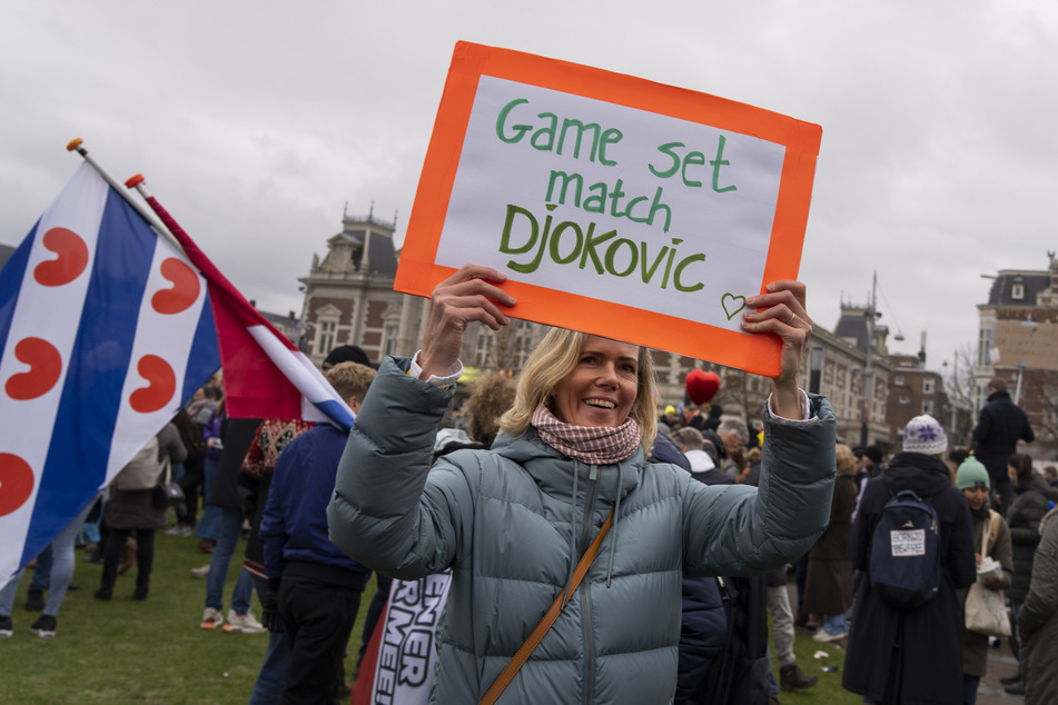 Niederlande, Amsterdam: Ein Protestteilnehmer hält während einer Demonstration gegen die Corona-Maßnahmen der Regierung ein Schild hoch, auf dem zu lesen ist "Game, Set, Match, Djokovic".