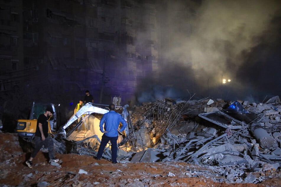 People and first responders stand on the rubble of a building destroyed in an Israeli air strike as a digger clears debris in the Haret Hreik neighborhood of Beirut's southern suburbs on Friday.