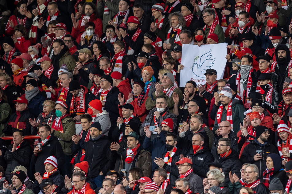 1. FC Union Berlin - FSV Mainz 05, 24. Spieltag, An der Alten Försterei: Ein Fan hält ein Plakat mit einer Friedenstaube. Zuschauer und Teams halten eine Schweigeminute in Gedenken an die Opfer des Ukraine Konfliktes.