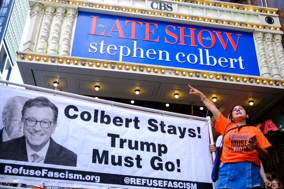 People protest with a banner reading "Colbert Stays! Trump Must Go!" outside the Ed Sullivan Theater in New York City on July 21, 2025.
