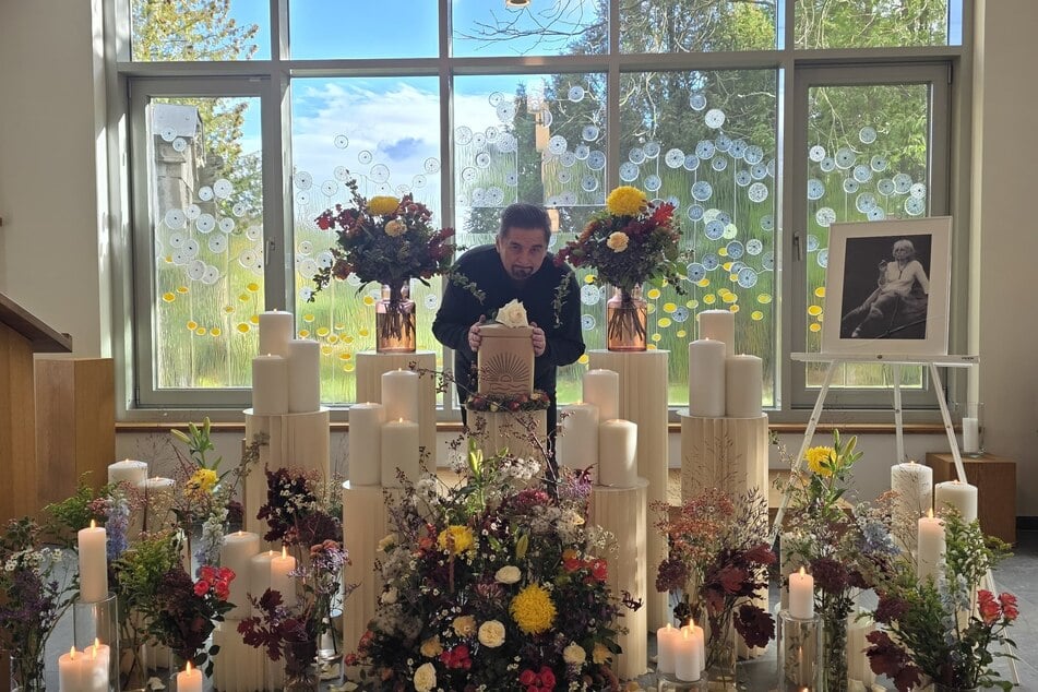 Bei der Trauerfeier wird die weiße Urne von vielen bunten Blumen umrahmt.