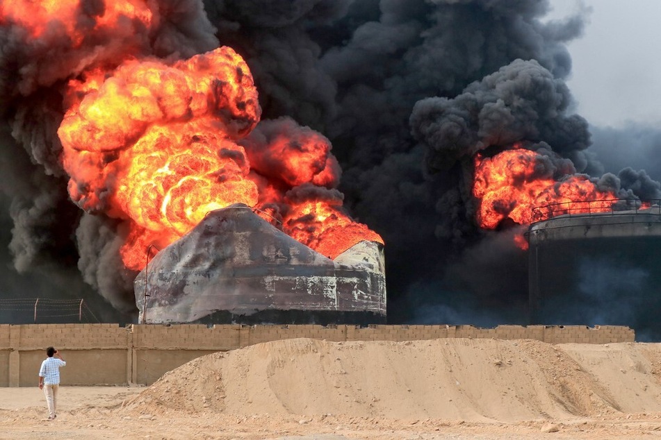 A man takes pictures of a raging fire at oil storage tanks a day after Israeli strikes on the port of Hodeida, Yemen.