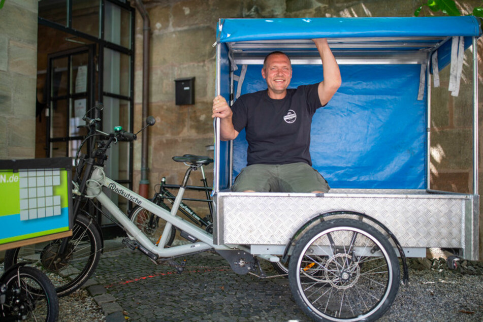 Andreas Reisch vom Cafe Hergricht, ein Verleih für Transporträder, sitzt zum Größenvergleich in einem Anhänger eines E-Lastenrads.