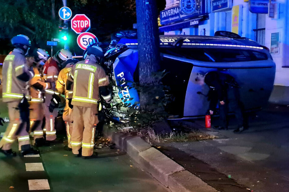 Feuerwehrleute kümmern sich um den verunglückten Polizeiwagen.