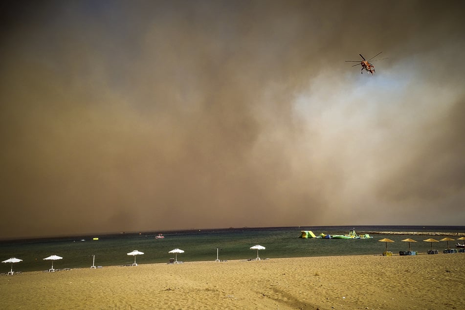 Ein Löschhubschrauber fliegt über einen Strand, während ein Waldbrand auf der griechischen Insel Rhodos wütet.