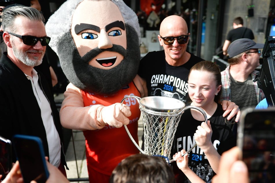 Präsident Sven Böttger (l.), Coach Rodrigo Pastore (51, r.) und "Karli" mit dem Europapokal. Das Ziel ist erreicht, auf die neue Halle für 10.000 Fans müssen die Chemnitzer noch bis 2030 warten.