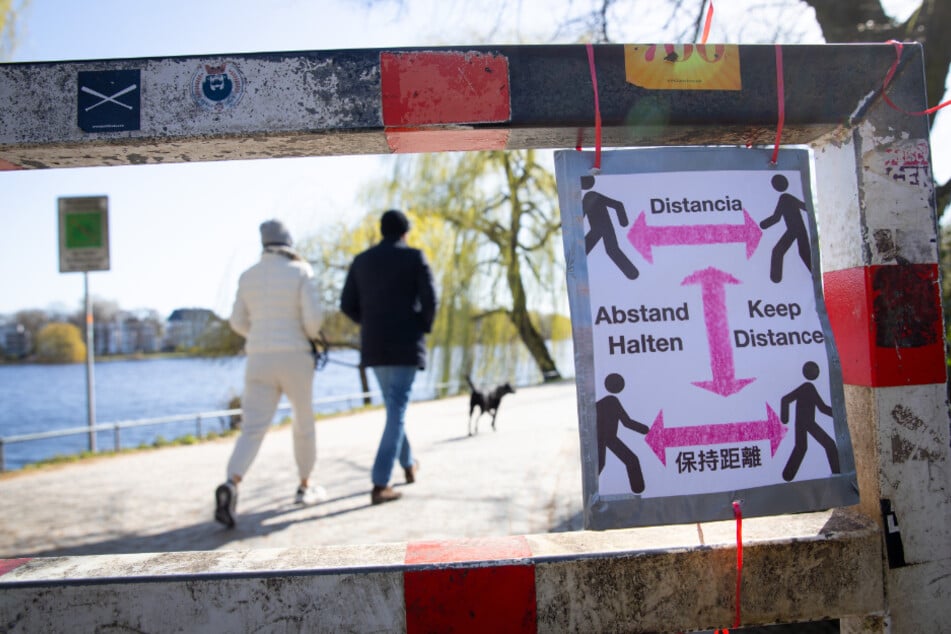 Ein selbstgebasteltes Schild mit der Aufschrift "Abstand Halten" in verschiedenen Sprachen ist am Beginn eines Weges um die Alster befestigt.