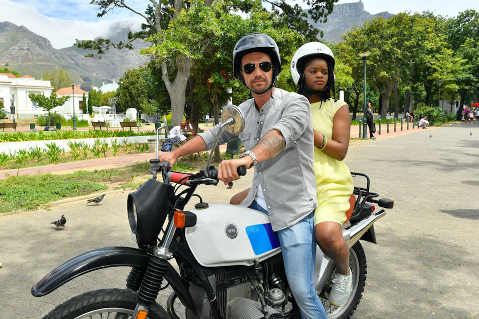 Kapitän Max Parger (Florian Silbereisen) und Lea Bremer (Melodie Wakivuamina) sitzen auf einem Motorrad - eine Szene aus "Das Traumschiff: Kapstadt".