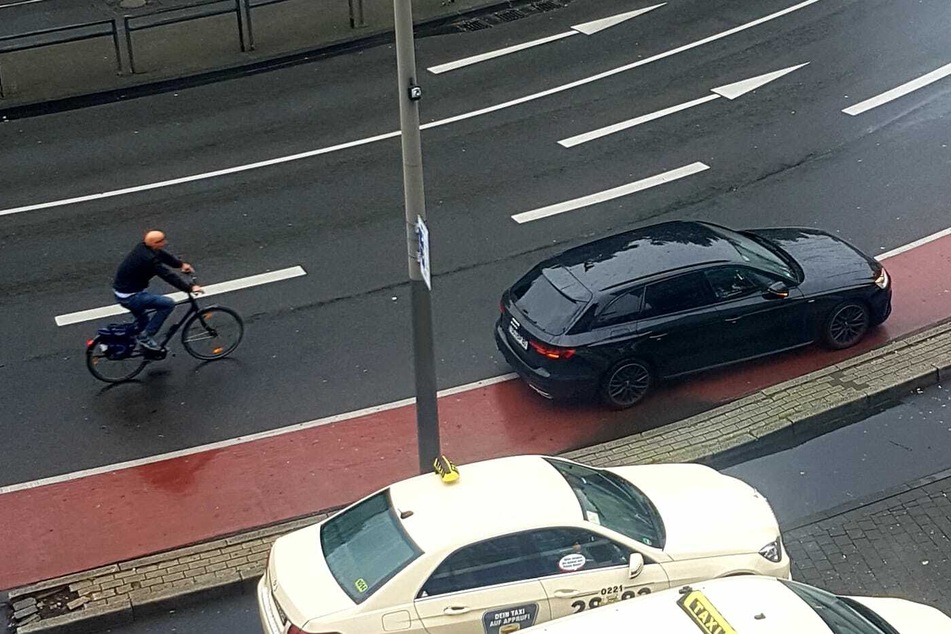 Ein Autofahrer am Neumarkt parkt auf dem mit einer durchgezogenen Linie abgetrennten Radstreifen. Ein Radfahrer muss ausweichen.
