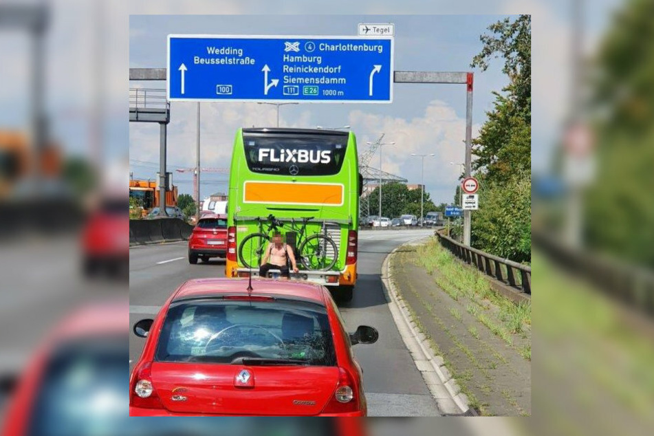Ein unbekannter Mann sitzt in aller Ruhe auf der Halterung für Fahrräder am Heck eines Flixbusses, der über die Berliner Stadtautobahn fährt.