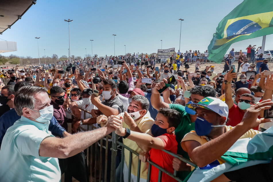 Sao Raimundo Nonato: Auf diesem vom brasilianischen Präsidentenamt zur Verfügung gestellten Bild schüttelt der vor wenigen Tagen wieder negativ auf Covid-19 getestete Präsident Jair Bolsonaro (l) Anhängern die Hand, als er auf dem Internationalen Flughafen Serra da Capivara ankommt.