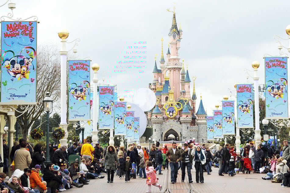 Besucher laufen auf der Main Street im Disneyland Paris. Im Hintergrund sieht man das Schloss des Freizeitparks.