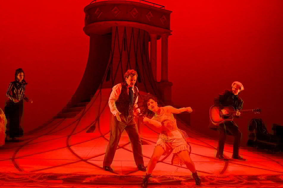 Nora Helmer (Karina Plachetka) tanzt in Unterwäsche zur Gitarrenbegleitung von Dr. Rank (Thomas Eisen, r.). Ehemann Torvald (Viktor Tremmel) und Freundin Christine (Betty Freudenberg, l.) sehen zu.