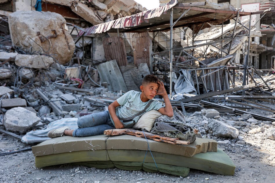 A boy lies on several foam mattresses by rubble outside a destroyed building in the centre of Khan Younis in the southern Gaza Strip on October 10, 2025.