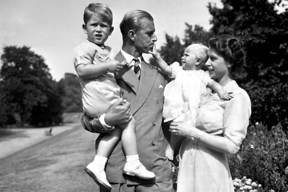 9. August 1951: Prinzessin Elizabeth (re.), die Prinzessin Anne in den Armen hält, und Prinz Philip, Herzog von Edinburgh, der Prinz Charles trägt, stehen auf dem Gelände von Clarence House.